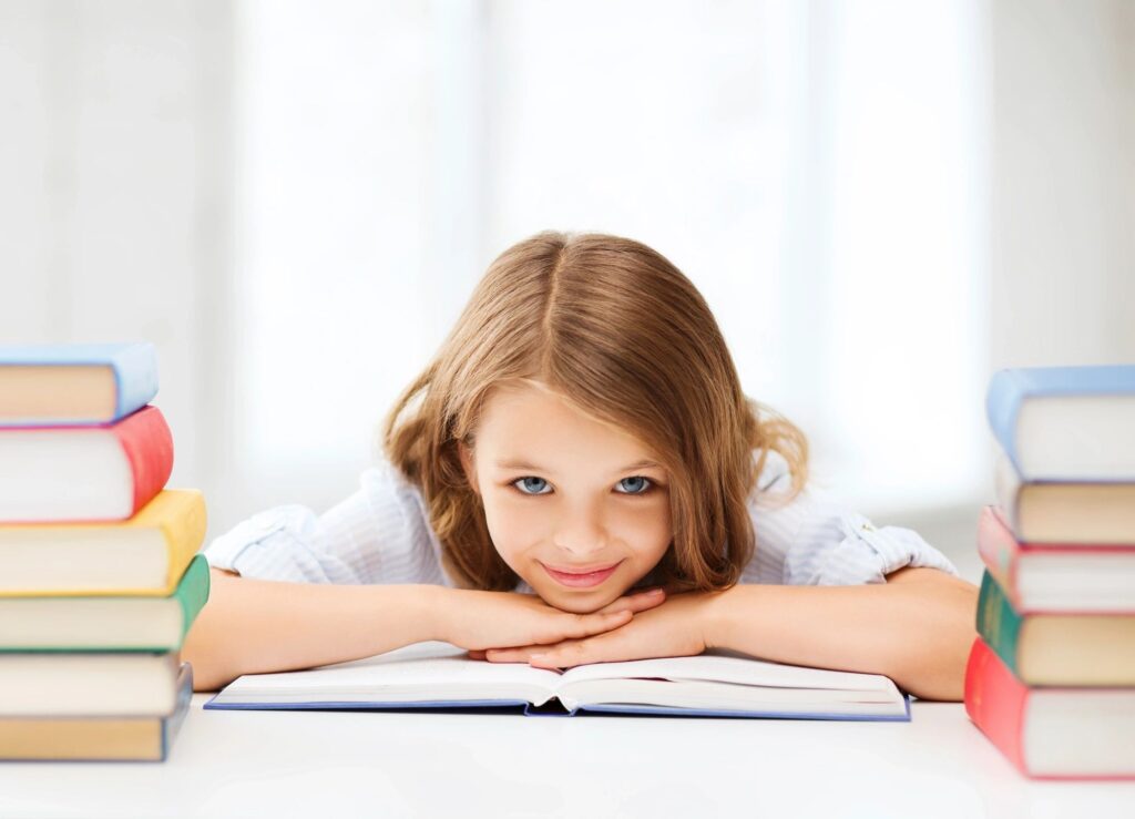 Photographie d'une jeune enfant, la tête et les deux mains posés sagement sur un livre ouvert. Elle est entourée de colonnes de livres.