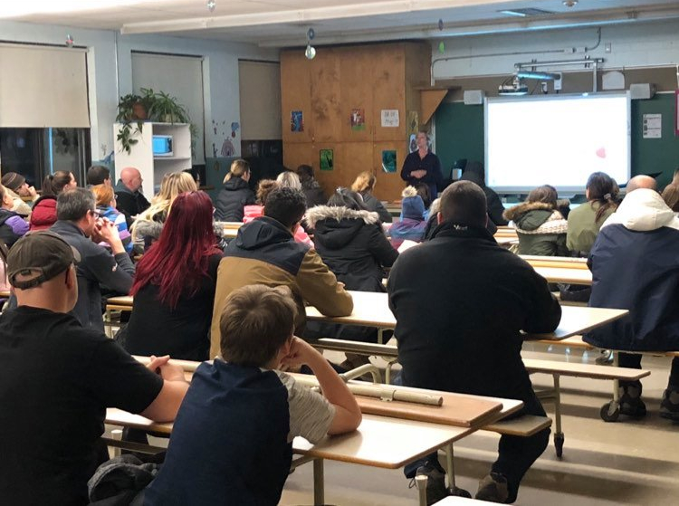 Photographie de Josée Bellehumeur devant une classe remplie de parents. Elle leur enseigne les stratégies du projet Le Pont, apprises par leurs enfants.