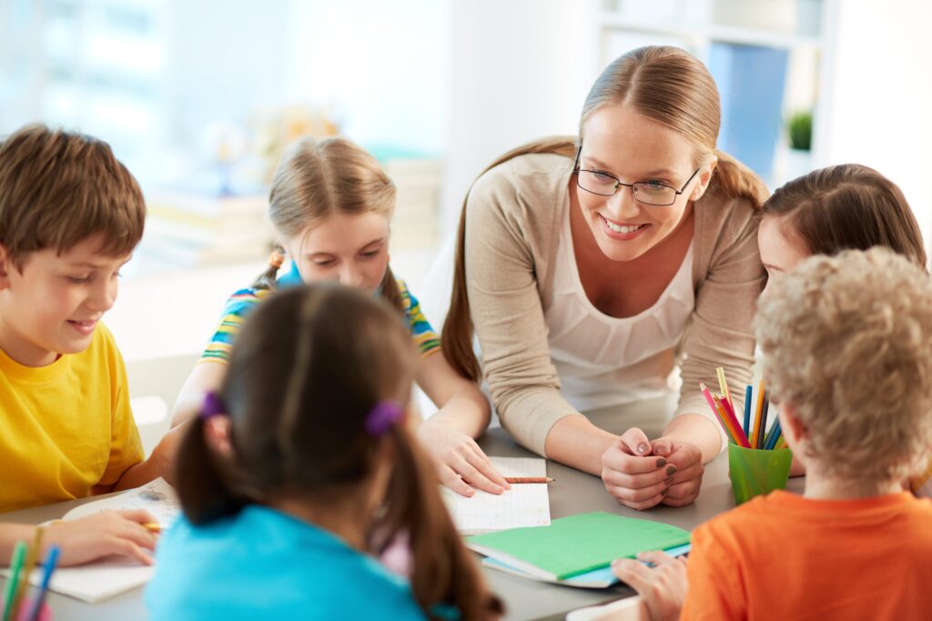 Photographie d'une jeune enseignante souriante entourée d'élèves attentifs.