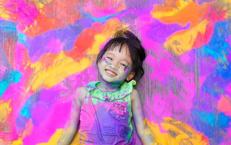 Photographie d'une jeune enfant couchée dans de la peinture colorée.
