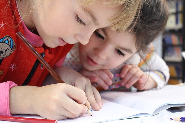 Photographie de deux enfants d'âge préscolaire qui écrivent dans un cahier d'activité.